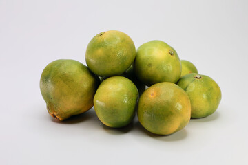 A Group Of Greenish Yellow Citrus Fruits, Possibly Unripe Mandarins or Limes. The Image Highlights The Natural Color Gradient And Freshness Of The Harvest.