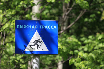 A Blue Square Sign In A Forest Featuring A Skier Symbol And Cyrillic Text "Lyzhnaya Trassa", Which Means Ski Trail. Concept Of Winter Sports Navigation.