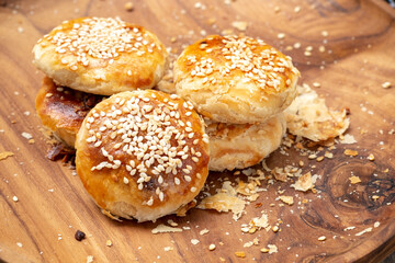 Traditional Indonesian bakpia pastry with mung bean filling on a wooden plate. Close-up high-angle shot of a flaky snack with crumbs and a checkered cloth detail.
