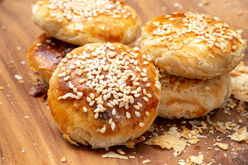 Traditional Indonesian bakpia pastry with mung bean filling on a wooden plate. Close-up high-angle shot of a flaky snack with crumbs and a checkered cloth detail.