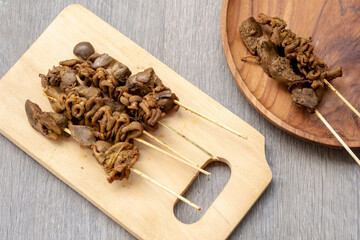 Tasty chicken intestine and liver skewers, known as sate jeroan, served on a wooden board and plate. These are classic Indonesian savory snacks.