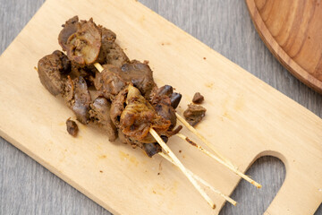 Savory chicken liver and gizzard skewers (sate ati ampela) on a wooden board. A classic Indonesian side dish often paired with Cianjur-style chicken porridge.