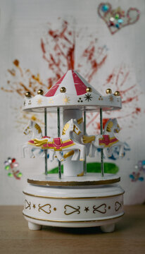 Horizontal capture of a white and pink carousel music box with gold details and tiny horses. Soft natural light highlights the textures, while a shallow depth of field creates a dreamy, nostalgic mood