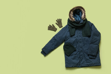 Stylish blue winter parka with hat, gloves and scarf on green background © Pixel-Shot