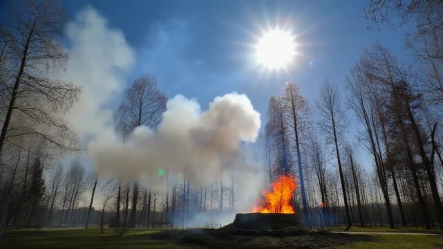 High clouds smoke fire in city park against blue sky, bright sun disk, lens flare, arson against of trees in spring.