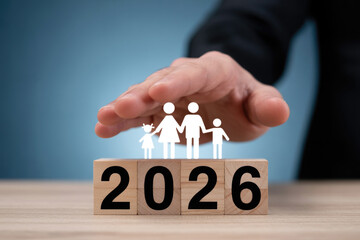 Family insurance, Hand protecting family figures resting on wooden blocks marked 2026 for future planning concepts.