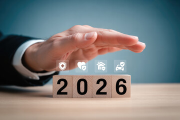 Family insurance, Hand protecting wooden blocks showing year 2026 with various insurance icons for financial planning.