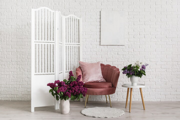 Cozy chair, folding screen and lilac flowers in vases in living room