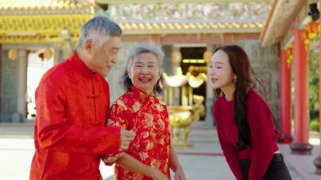 Young asian girl dressed in traditional Chinese clothing joyfully receives red envelopes from her parents at a lovely temple, marking a heartfelt New Year celebration filled with culture and love