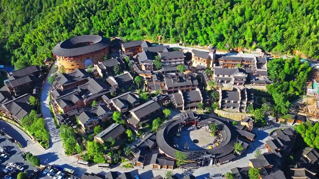 Aerial shot of traditional round earthen building and ancient village architecture surrounded by lush green forest. The famous Wangxiang Valley Scenic Area is located in Jiangxi, China.