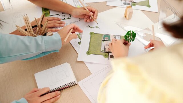 Architect and engineer use tree model discuss about building blueprint on table with architectural document, measurement tools and wooden block scatter around at modern office. Closeup. Delineation.