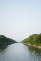 Obraz premium Serene river flowing between lush green trees under a tranquil sky.