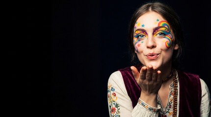 Woman with rainbow face paint and a white vest. She is blowing a