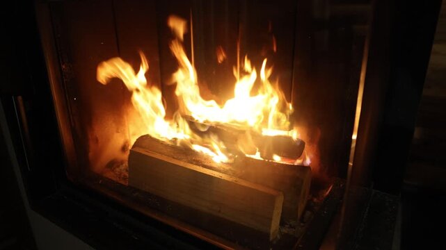 Close-up of a warm, crackling fire inside a modern glass-enclosed fireplace, with flames dancing over stacked firewood logs