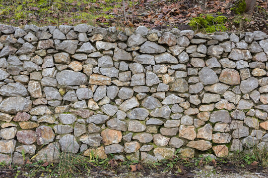 Kamienny mur z nieregularnych polnych kamieni &ndash; tło ogrodowe, suchy murek i naturalna struktura ściany.