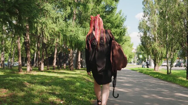 woman strolling with umbrella calmly, tranquil female figure with umbrella moves gradually through park, gentlehaired woman with vibrant dreadlocks slowly walks beneath sunlit trees in park