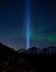 Night sky over mountains with a bright, vertical blue light