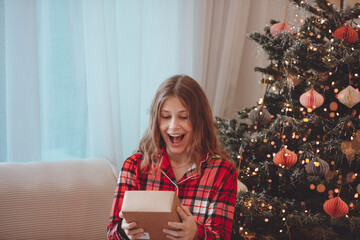 Young Woman Unwrapping Christmas Gift By Decorated Tree