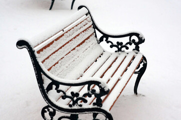 しんしんと降り積もる雪に覆われた公園のベンチ。静かな冬の日の屋外風景。