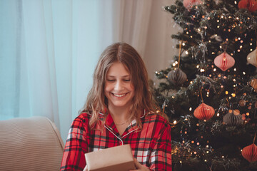 Young Woman Unwrapping Christmas Gift By Decorated Tree