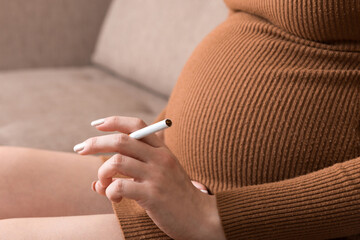 Close-up of pregnant woman is holding a cigarette sitting on sofa at home
