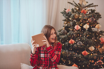 Young Woman Unwrapping Christmas Gift By Decorated Tree