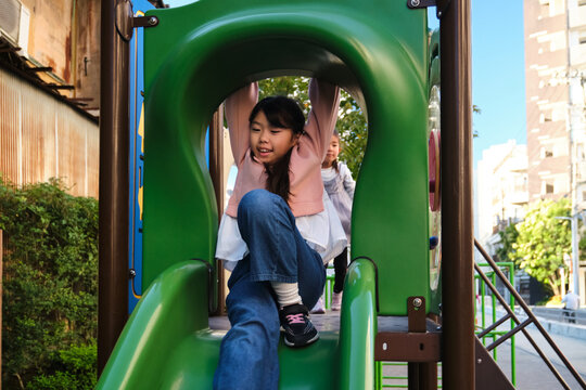 Japanese girl playing on playground slide in park