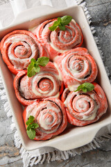 Close-up of pink cinnamon rolls with white icing in a baking dish on a table. Vertical top view from above
