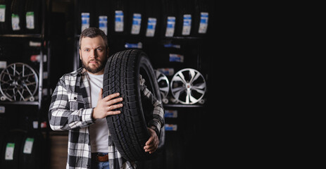 Caucasian male adult holding winter tire in auto shop setting, dark banner tyre store © Parilov