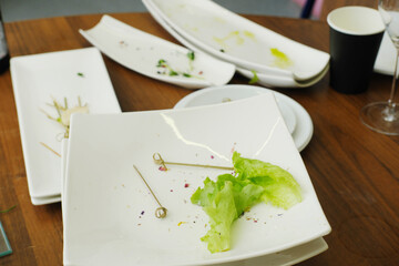 Dirty dishes piled on a wooden table after a banquet, featuring leftover food scraps, empty plates, and utensils, showcasing the aftermath of a festive reception with vibrant colors