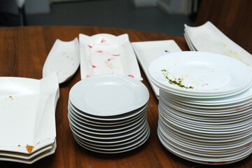Stacked dirty plates and empty serving dishes after a banquet, showcasing leftover food remnants on a wooden table, emphasizing post-event cleanup and dining aftermath