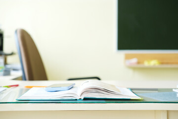 Open textbook on a desk with stationery items, a smartphone, and a blurred chair in the background, creating a study environment with copy space for educational content