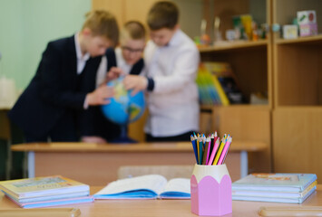 Group of three boys engaged in learning about geography with a globe in a classroom, surrounded by educational materials and colorful stationery, showcasing collaborative study