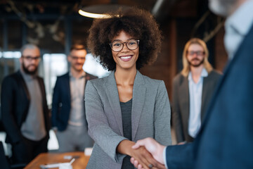 Black Female chief shaking hands with business partner while standing with her team of experts at office