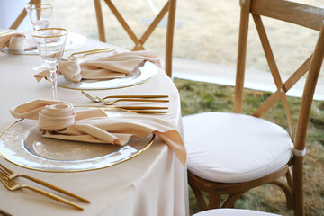 Elegant wedding banquet table setting featuring gold-accented plates, soft fabric napkins, crystal glassware, and wooden chairs, creating a sophisticated dining atmosphere with copy space