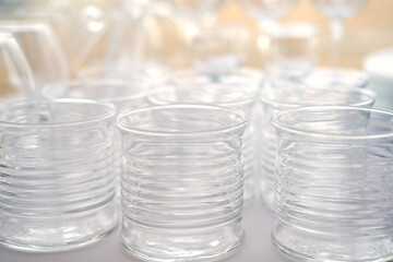 Clear glass cups arranged closely together on a surface with reflections and highlights, featuring ribbed texture and varying heights in a bright setting
