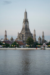 Fototapeta premium Morning sunlight hits Wat Arun temple in Bangkok, Thailand, with modern city buildings visible behind the historic riverside structure, Thailand - 22 Nov 2025.