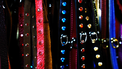 Collars in various colors including red, brown, black, and blue hanging on hooks with metal studs and buckles visible in a close-up arrangement