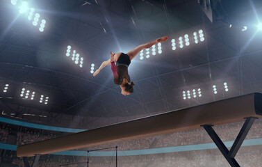 A gymnast performs a difficult trick on a balance beam.