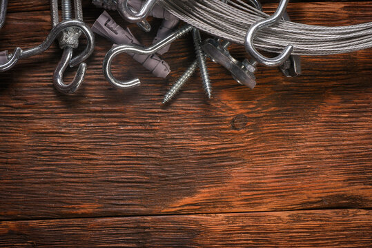 Hardware fasteners and steel wire rope with turnbuckles on wooden background.