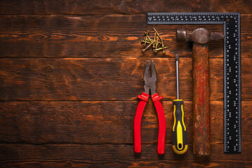 Hand tools set including hammer pliers screwdriver screws and metal square ruler in flat lay composition with copy space on wooden workbench table background.