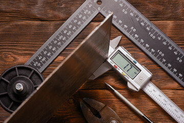 Digital caliper measuring metal sheet with steel ruler and metal scribe on wooden workbench table close up background.