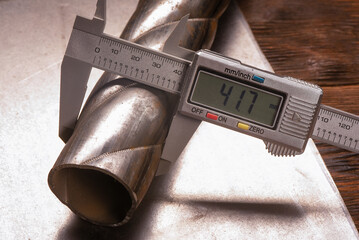 Digital caliper measuring metal pipe diameter on metal sheet on wooden workbench table background.
