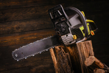 Naklejka premium Chainsaw with mounted guide bar and cutting chain and cut firewood logs on wooden workbench table background. Front view.