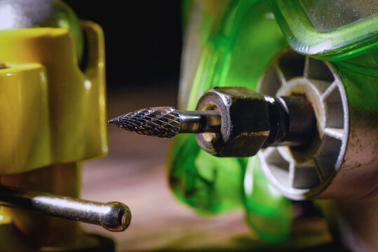 Electric straight grinder with metal burr bit fixed in clamp on wooden workbench table close up background.