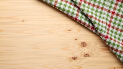 Green white and red checkered tablecloth diagonally folded over a natural light wooden background with visible grain and knots offering copy space