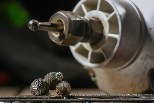 Electric straight grinder with metal milling cutter attachments for metalworking on wooden workbench table close up background.