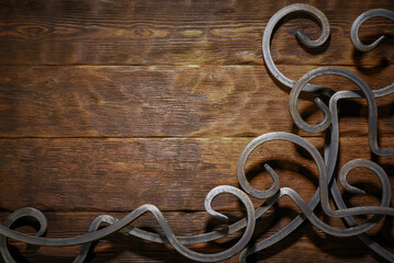 Forged metal scrollwork ornament decorative on dark wooden plank workbench table top view background.