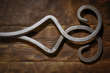 Forged metal scrollwork ornament decorative on dark wooden plank workbench table top view background.