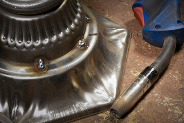 Metal welded lamp base on background with forged hook and welding torch resting on workshop floor background.